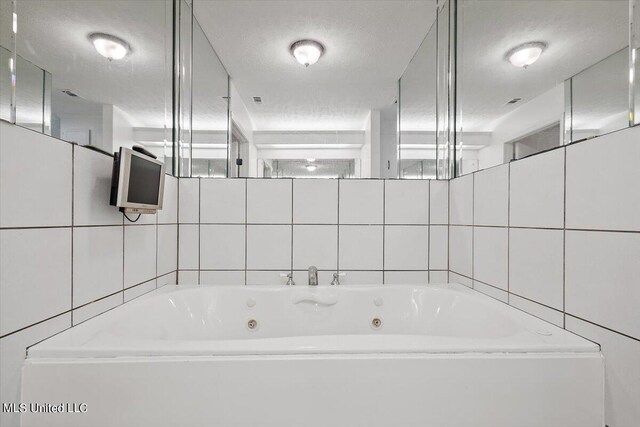 bathroom with tile walls, a textured ceiling, and a jetted tub