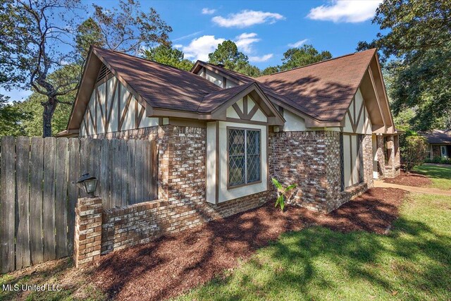 view of side of property with a lawn, fence, a shingled roof, and brick siding
