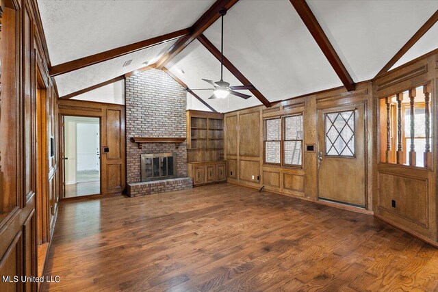 unfurnished living room featuring ceiling fan, wood walls, dark hardwood / wood-style floors, a fireplace, and lofted ceiling with beams