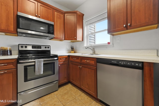 kitchen featuring light tile patterned floors, brown cabinets, stainless steel appliances, light countertops, and a sink