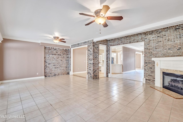 unfurnished living room featuring ceiling fan, a high end fireplace, brick wall, crown molding, and light tile patterned flooring