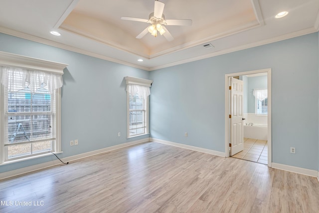 empty room with a tray ceiling, ceiling fan, light hardwood / wood-style flooring, and ornamental molding