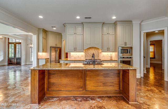 kitchen featuring ornamental molding, appliances with stainless steel finishes, light stone counters, and an island with sink