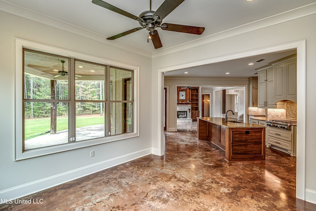 kitchen with light stone counters, ornamental molding, an island with sink, cream cabinetry, and decorative backsplash