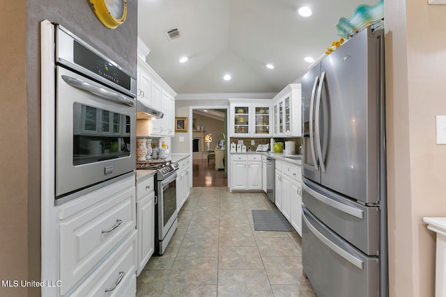 kitchen with vaulted ceiling, stainless steel appliances, white cabinets, and tasteful backsplash