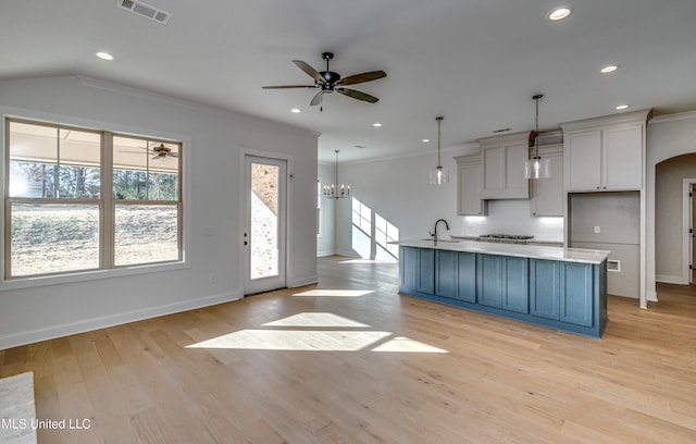 kitchen featuring decorative light fixtures, light hardwood / wood-style floors, backsplash, a center island with sink, and crown molding