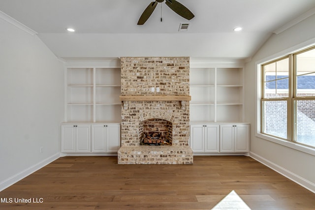 unfurnished living room featuring built in shelves, a brick fireplace, light hardwood / wood-style flooring, and a healthy amount of sunlight