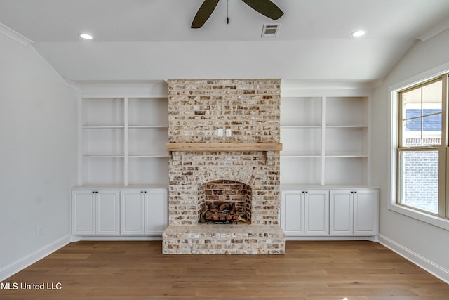 unfurnished living room featuring a fireplace, built in features, a healthy amount of sunlight, and light hardwood / wood-style flooring