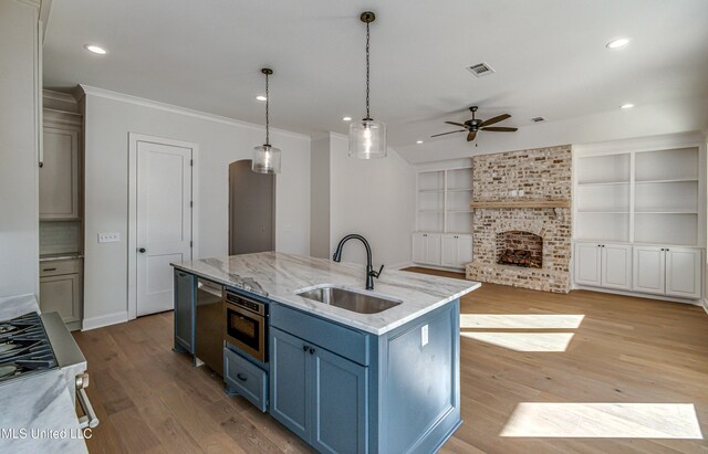 kitchen with a kitchen island with sink, sink, decorative light fixtures, blue cabinets, and built in features