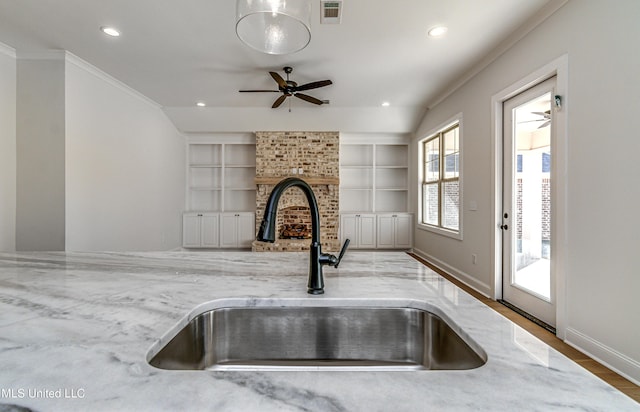 kitchen featuring light stone countertops, hardwood / wood-style floors, sink, built in features, and a brick fireplace