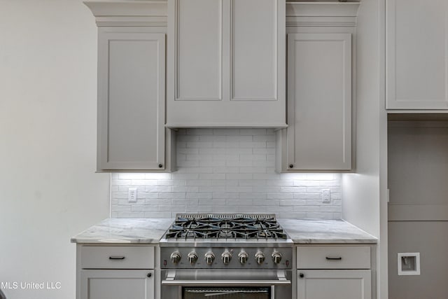 kitchen with light stone counters, stainless steel range, white cabinets, and tasteful backsplash