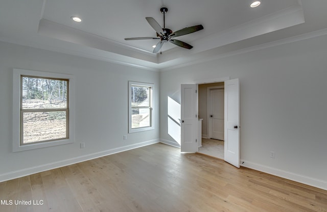 empty room featuring light wood-type flooring, a tray ceiling, and ornamental molding