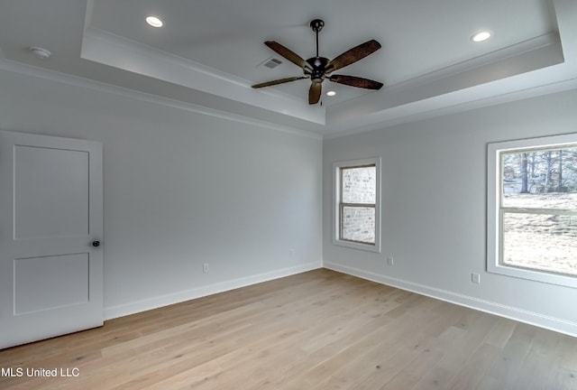 empty room with light wood-type flooring, a healthy amount of sunlight, crown molding, and a tray ceiling