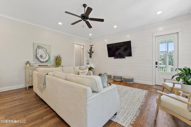 living room with dark wood-type flooring, ceiling fan, wood walls, and crown molding