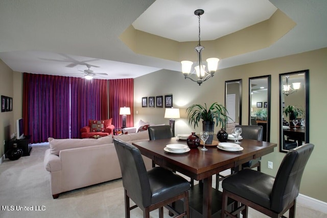 carpeted dining room featuring ceiling fan with notable chandelier and a raised ceiling