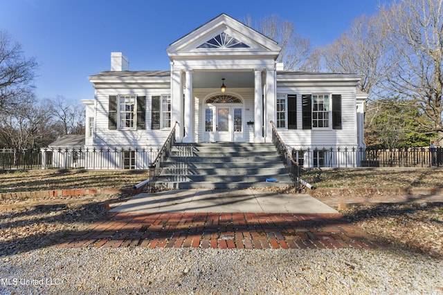 greek revival house with covered porch, fence, and a chimney