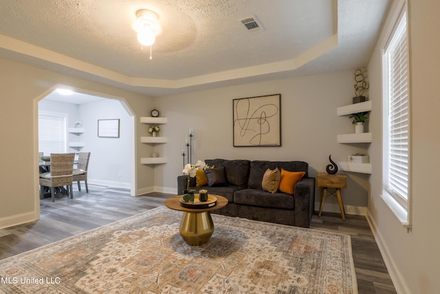 living room featuring a raised ceiling, built in features, dark hardwood / wood-style floors, and a textured ceiling