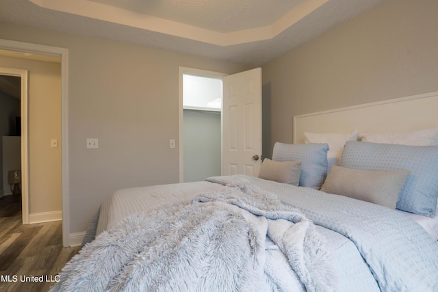 bedroom with dark hardwood / wood-style flooring, a textured ceiling, a raised ceiling, a spacious closet, and a closet