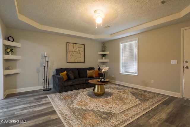 living room with built in shelves, a textured ceiling, a tray ceiling, and dark hardwood / wood-style floors