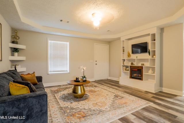 living room with a tray ceiling, built in features, a textured ceiling, and hardwood / wood-style flooring