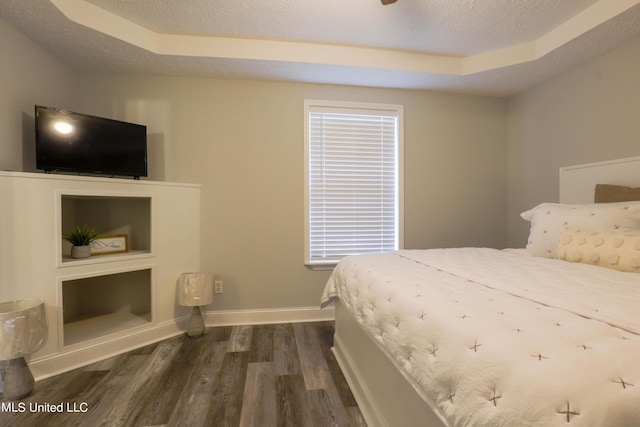 bedroom featuring a raised ceiling, a textured ceiling, and dark hardwood / wood-style floors