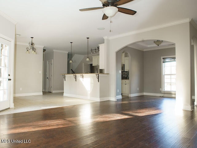 unfurnished living room with crown molding, ceiling fan with notable chandelier, and hardwood / wood-style flooring