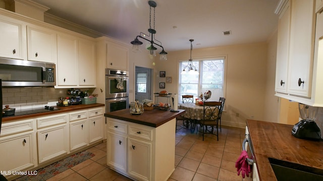 kitchen with appliances with stainless steel finishes, decorative light fixtures, light tile patterned floors, butcher block countertops, and tasteful backsplash