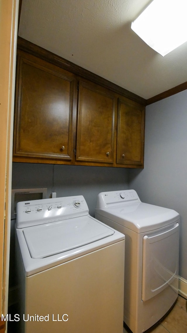 laundry area featuring light tile patterned floors, a textured ceiling, cabinets, and washing machine and clothes dryer