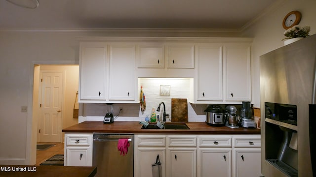 kitchen with appliances with stainless steel finishes, sink, butcher block countertops, white cabinets, and ornamental molding