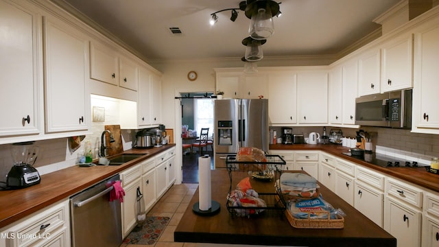 kitchen with appliances with stainless steel finishes, white cabinetry, light tile patterned flooring, sink, and butcher block countertops