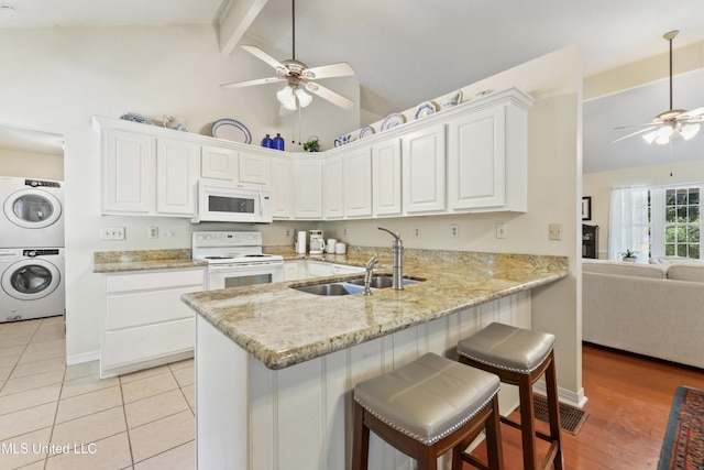 6658 Ahekolo Cir, Diamondhead, MS 39525 - kitchen featuring white appliances, a ceiling fan, stacked washing machine and dryer, white cabinets, and a peninsula