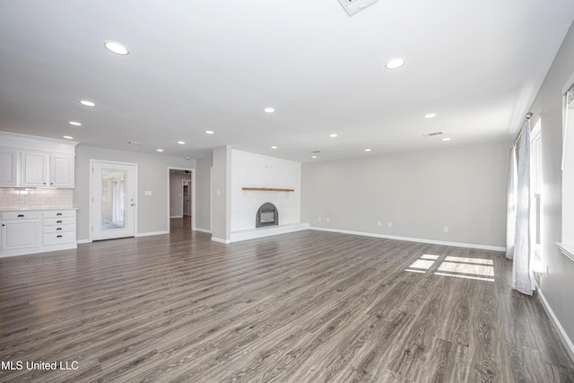 unfurnished living room with a brick fireplace, a healthy amount of sunlight, and dark hardwood / wood-style flooring