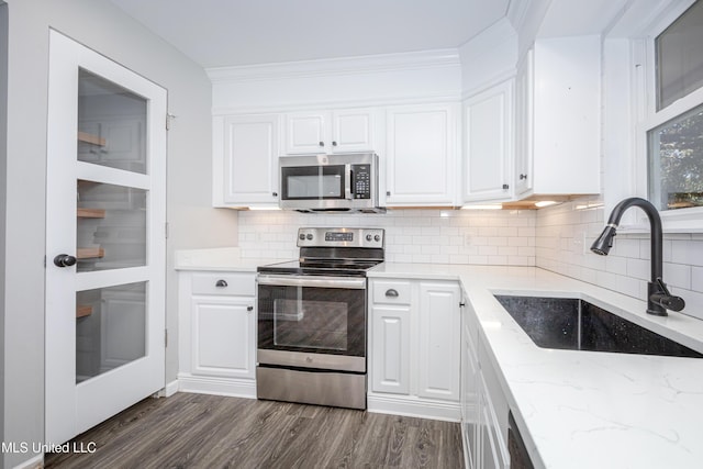 kitchen featuring appliances with stainless steel finishes, dark wood-type flooring, white cabinets, decorative backsplash, and sink