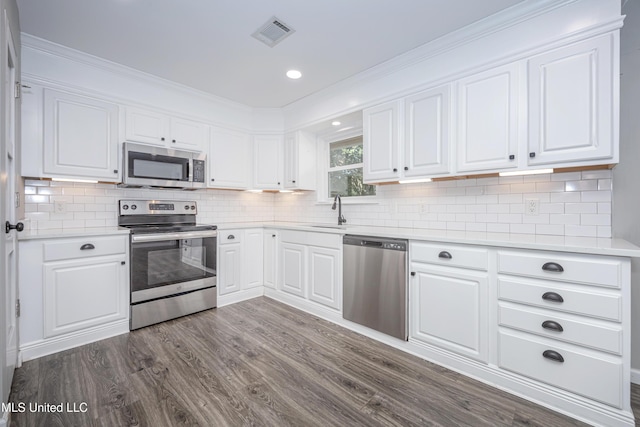 kitchen featuring sink, backsplash, dark wood-type flooring, appliances with stainless steel finishes, and white cabinets