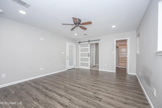 unfurnished bedroom with a closet, a spacious closet, ceiling fan, dark hardwood / wood-style flooring, and a barn door