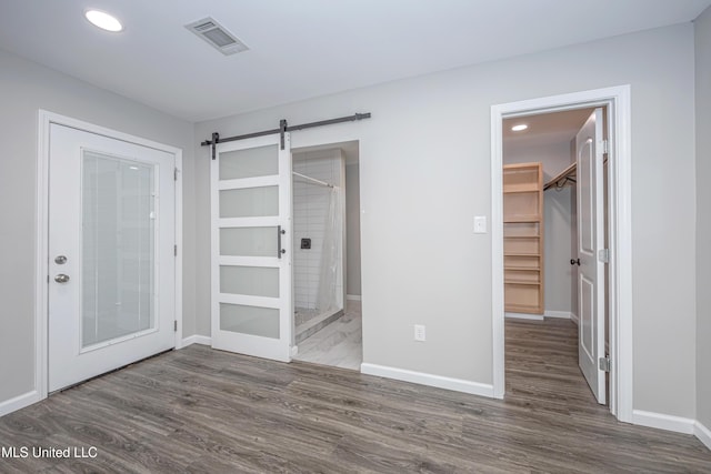 unfurnished bedroom featuring a closet, ensuite bath, a spacious closet, dark hardwood / wood-style flooring, and a barn door