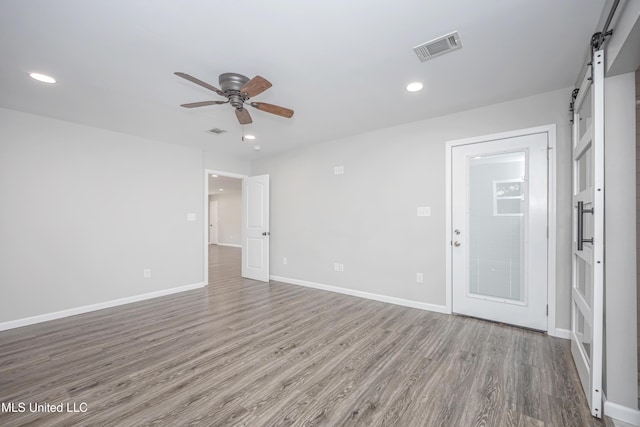 unfurnished room with hardwood / wood-style floors, ceiling fan, and a barn door