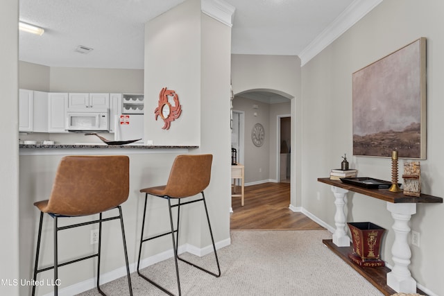 kitchen featuring a breakfast bar, a textured ceiling, white cabinetry, crown molding, and light hardwood / wood-style flooring