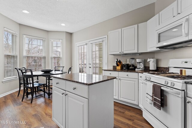 kitchen featuring hardwood / wood-style floors, a textured ceiling, white cabinetry, a center island, and white appliances