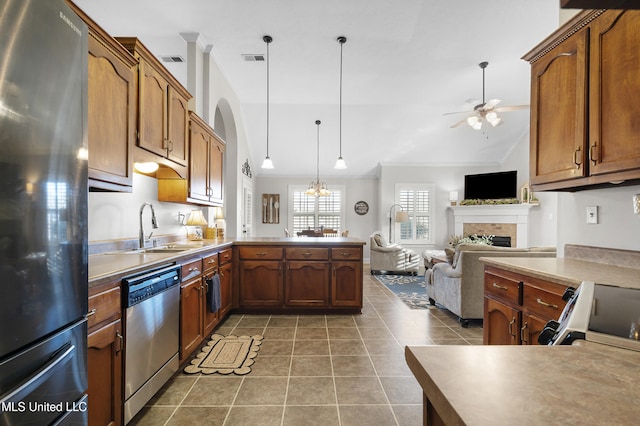 kitchen with sink, crown molding, a brick fireplace, pendant lighting, and stainless steel appliances