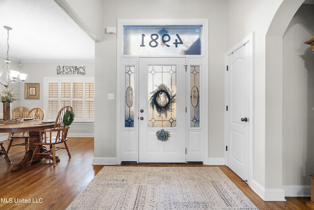 foyer featuring wood-type flooring, a notable chandelier, and crown molding