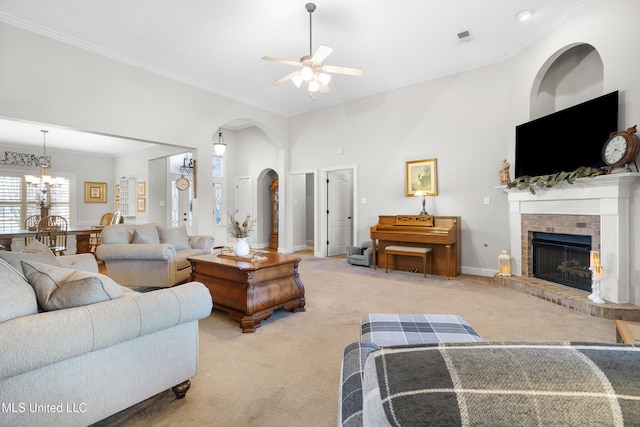 carpeted living room with a brick fireplace, ornamental molding, ceiling fan, and a high ceiling