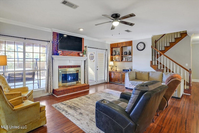 living room with dark wood-type flooring, crown molding, a fireplace, and ceiling fan