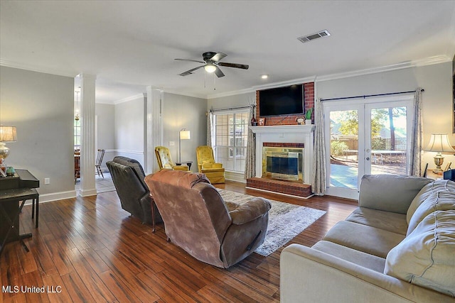 living room with crown molding, a brick fireplace, decorative columns, and dark hardwood / wood-style flooring