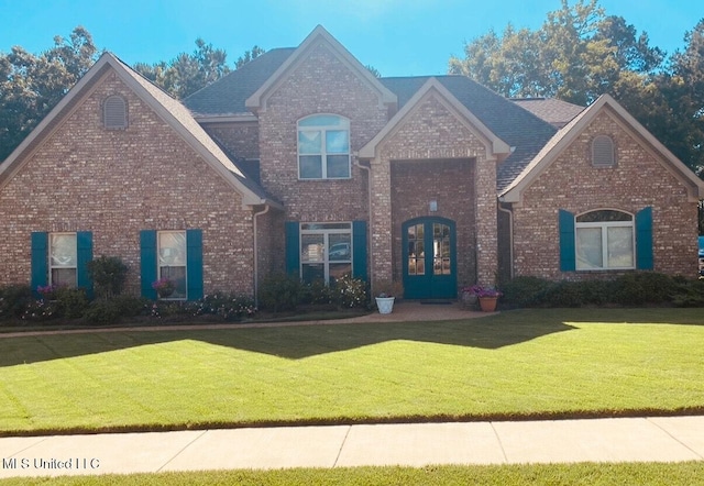 view of front of house with french doors, brick siding, and a front lawn