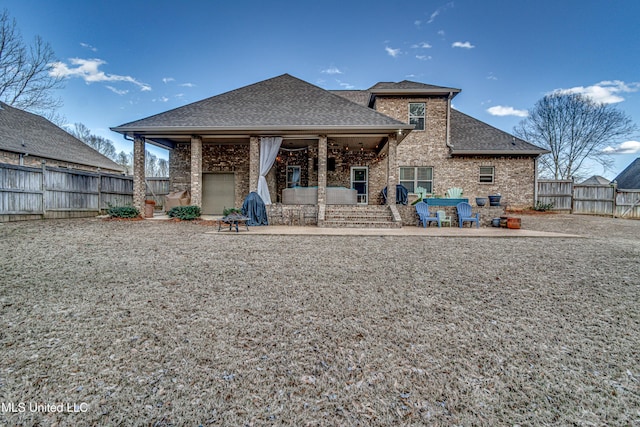 rear view of house featuring a shingled roof, a patio area, brick siding, and a fenced backyard