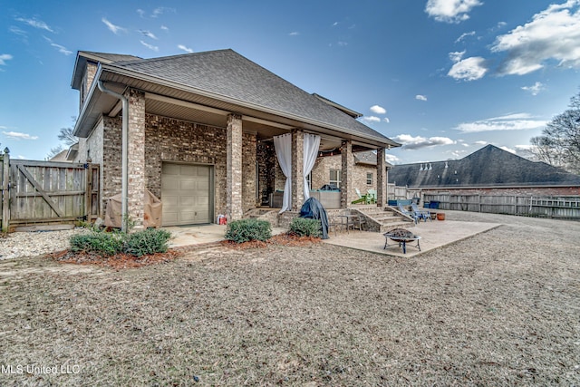 rear view of property featuring roof with shingles, brick siding, an outdoor fire pit, a patio area, and fence