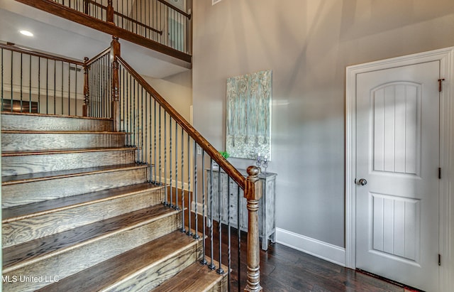 stairs with wood finished floors, a towering ceiling, and baseboards