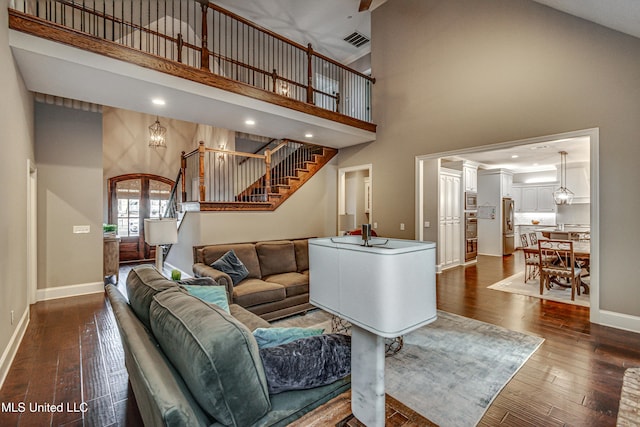 living area with dark wood-style floors, a high ceiling, baseboards, and stairs