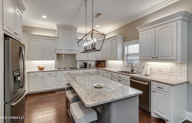 kitchen with visible vents, custom range hood, appliances with stainless steel finishes, a kitchen bar, and a sink